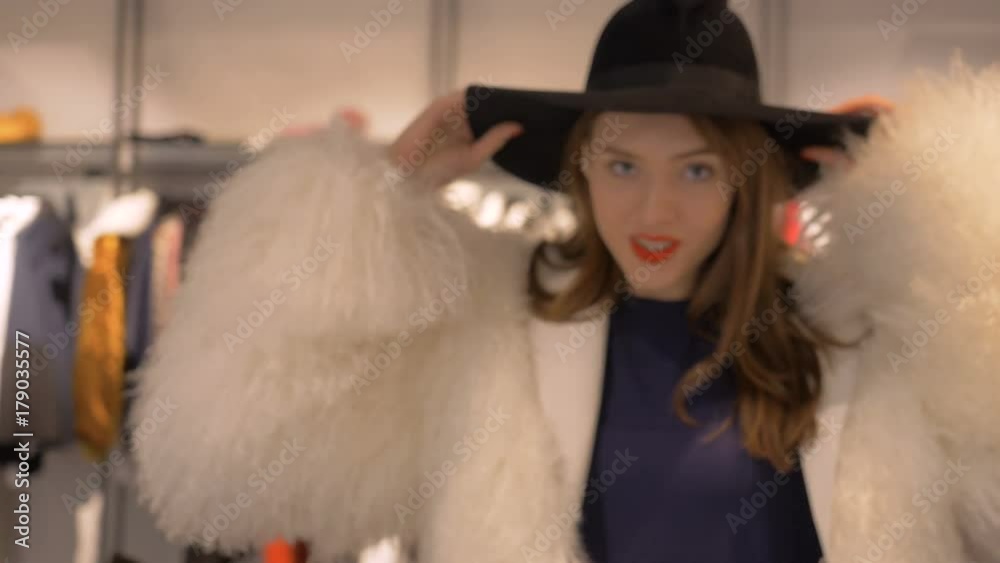 A cute girl tries on a hat in a luxury boutique. Model posing on camera. A cute girl tries on a hat in a luxury boutique. Model posing on camera.