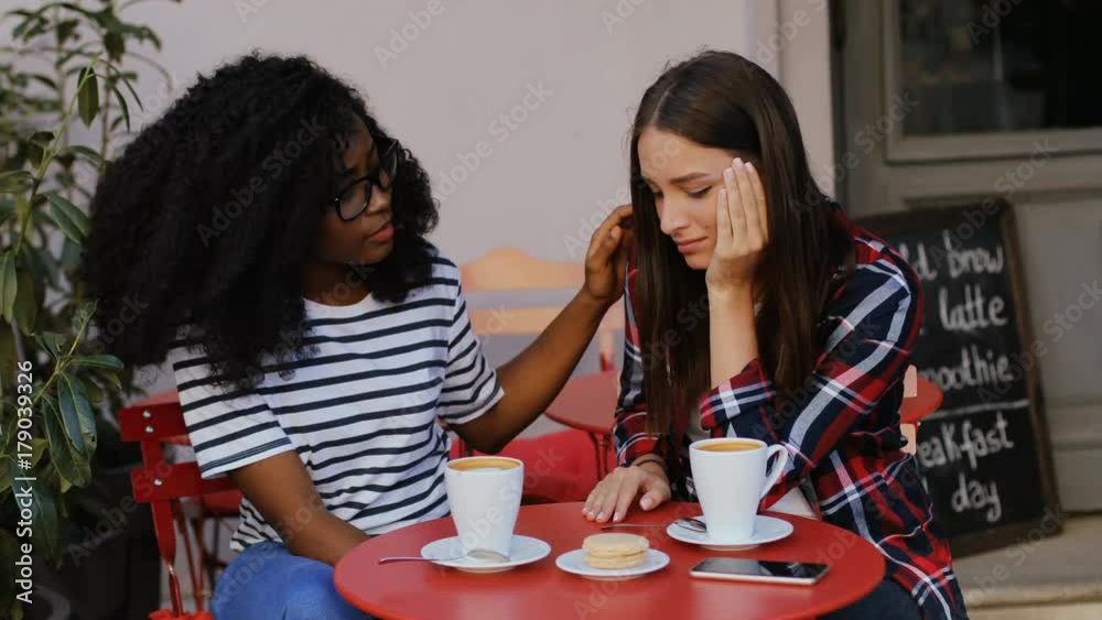 Young African pretty woman with curly hair talking with disappointed nice friend on terrace. Young woman crying. Young African pretty woman with curly hair talking with disappointed nice friend on terrace. Young woman crying.