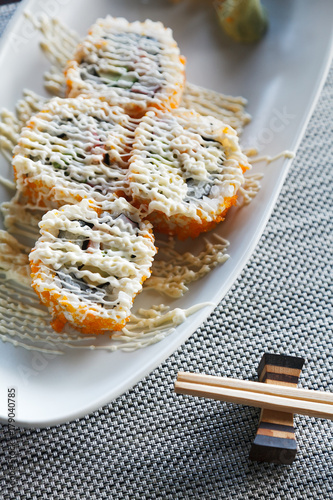 Sushi california rolls with topping mayonnaise on ellipse white plate on mat and chopstick beside