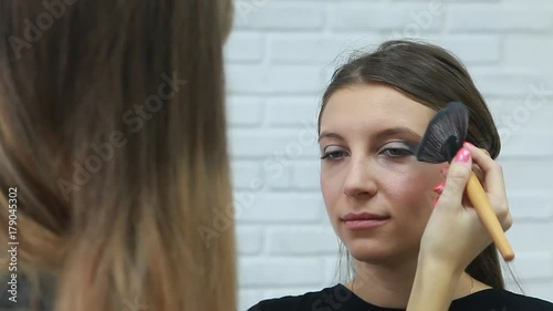 Woman is doing facial cosmetic makeup using face powder rouge brush to a model to create blush cheek.Beauty salon