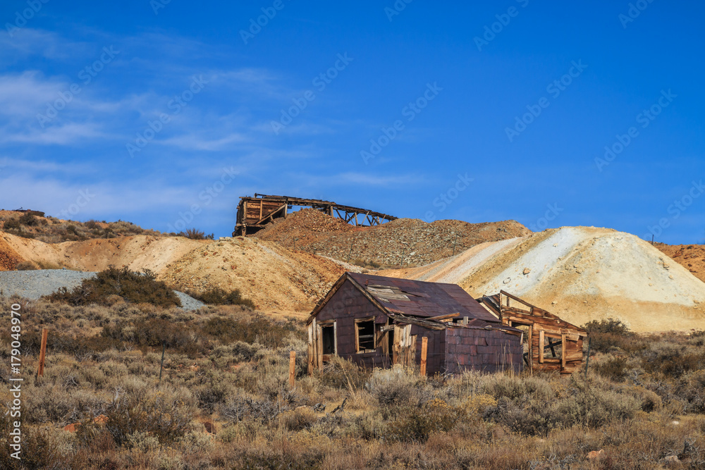 Old abandoned buildings and mining equipment in western 19th century gold town. Piles of shag from the mines are in the background. Blue sky with wispy clouds. Old abandoned buildings and mining equipment in western 19th century gold town. Piles of shag from the mines are in the background. Blue sky with wispy clouds.