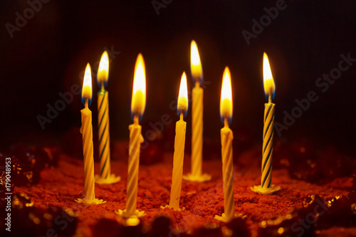 Candles are burning on a birthday cake on dark background. Selective focus