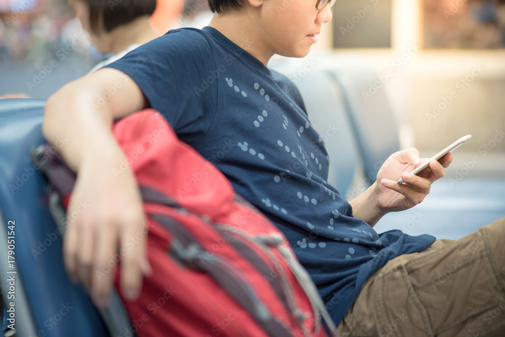 Young Asian man traveler with red backpack using smartphone in airport terminal, travel lifestyle in transportation building concept