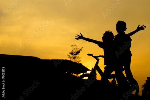 Kids On Bicycle In Silhouette Against Sunset 