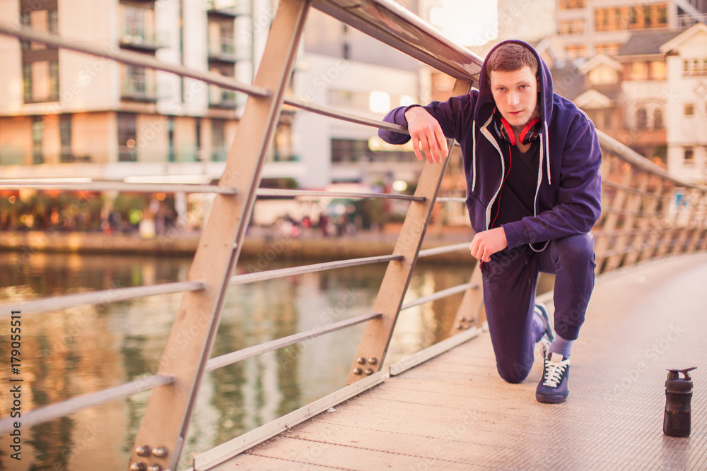 The young sporty man sitting on one knee outdoor relying on the railings