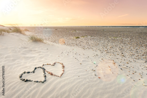 Pebbles arranged in shape of two hearts on sand beach ripples with beautiful sunset.