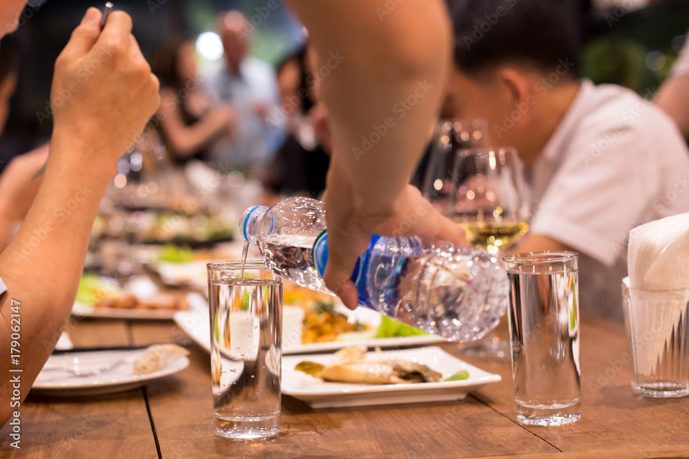 Candid waiter pouring water from bottle while people having dinne Candid waiter pouring water from bottle while people having dinne