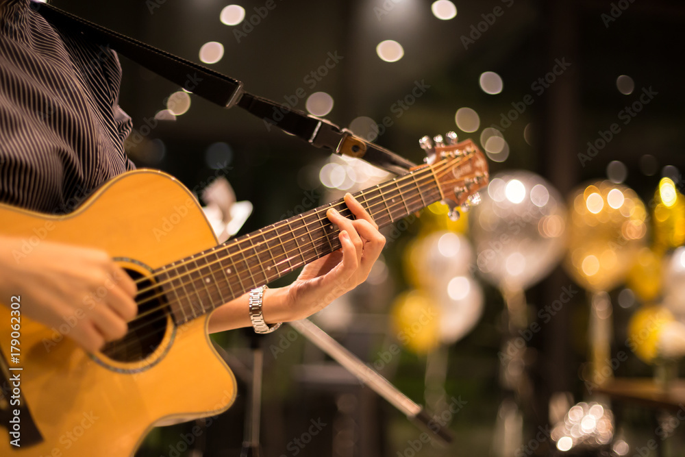 Fototapeta premium Kobieta bawić się gitarę akustyczną w barze przy nocą strzelał z wysokim iso z bokeh światłem