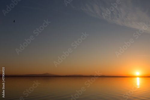 Foto Classic sunset on a lake, with sun low on the horizon and flying birds