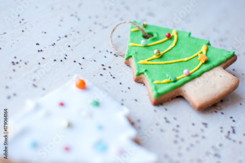 Two gingerbread cookies in the shape of the green and white Christmas tree on the background of a wooden table and scattered chia seeds.