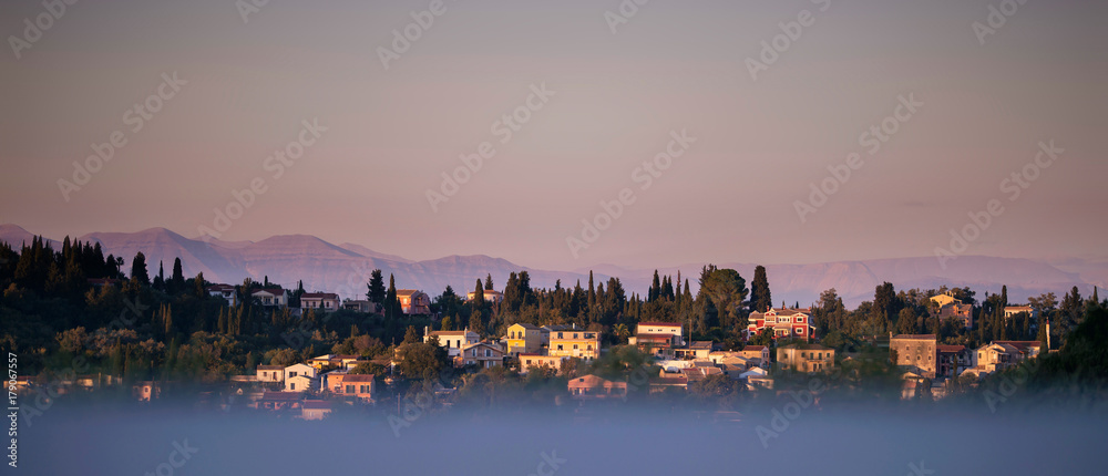 Skyline of mountains and hills with houses at sunset. Corfu island, Greece.