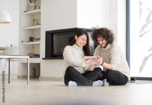 multiethnic couple using tablet computer in front of fireplace