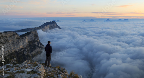 A man looking over a sea of clouds in the mountains at dawn. Vercors, France. © sanderstock