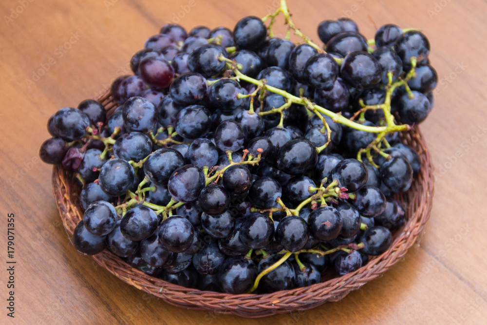 Ripe grapes in wicker basket on wooden table Ripe grapes in wicker basket on wooden table