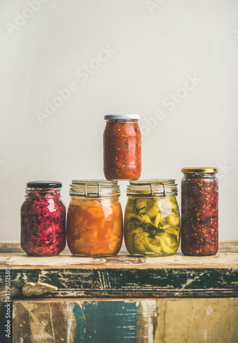 Autumn seasonal pickled or fermented colorful vegetables in jars over vintage kitchen drawer, white wall background, copy space, vertical composition. Fall home food preserving or canning