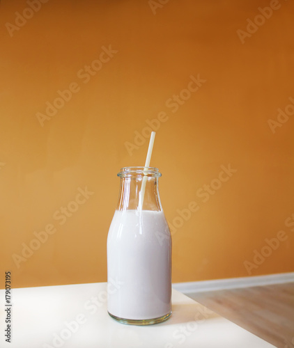 Milkshake with straw on white table and orange background