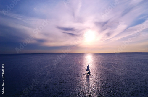 Fototapeta Romantic frame: yacht floating away into the distance towards the horizon in the rays of the setting sun