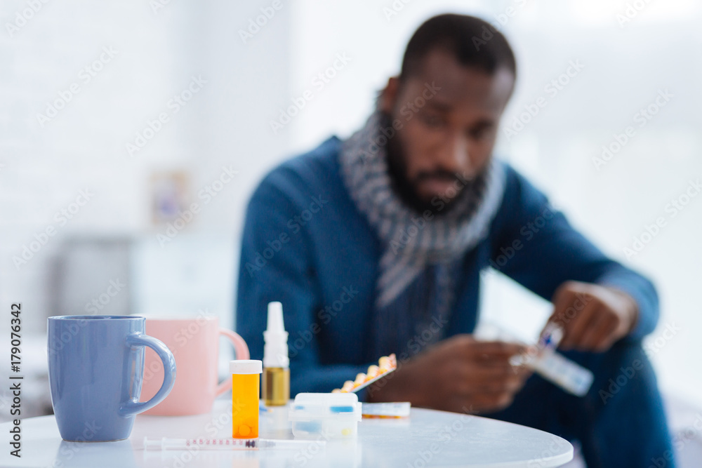 Sad ill man looking at the pills on his table Sad ill man looking at the pills on his table