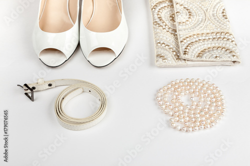 Female white shoes, bag, belt and pearl necklace on a white background