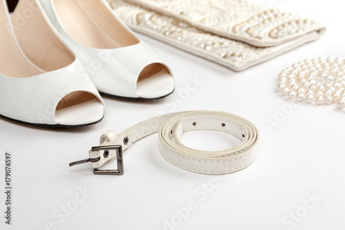 Female white shoes, bag, belt and pearl necklace on a white background