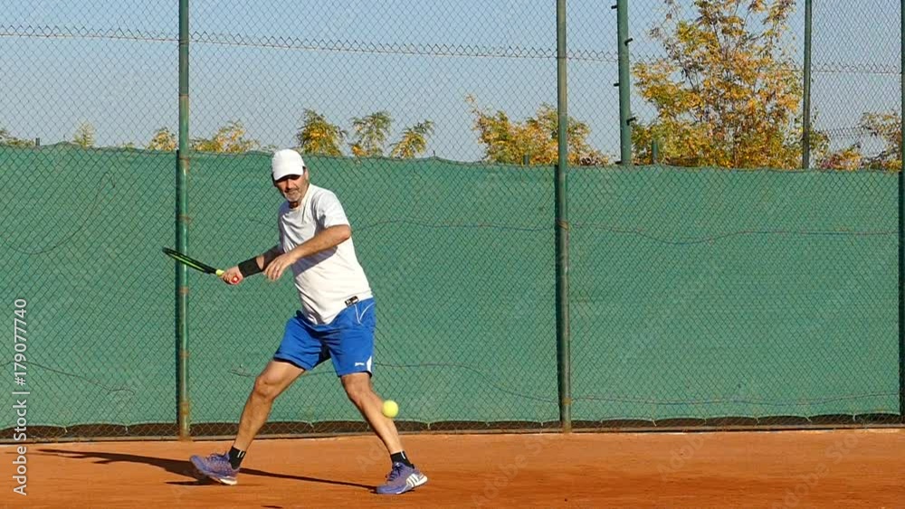 Mature man playing tennis on clay court, slow motion Mature man playing tennis on clay court, slow motion