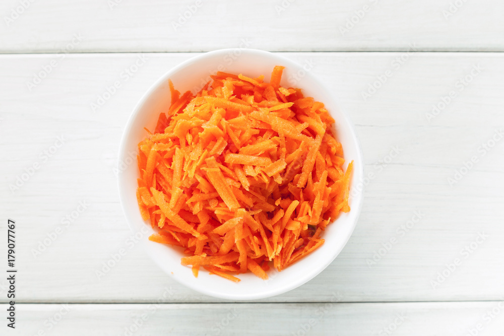 Grated fresh carrot in a white ceramic bowl top view