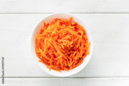 Grated fresh carrot in a white ceramic bowl top view