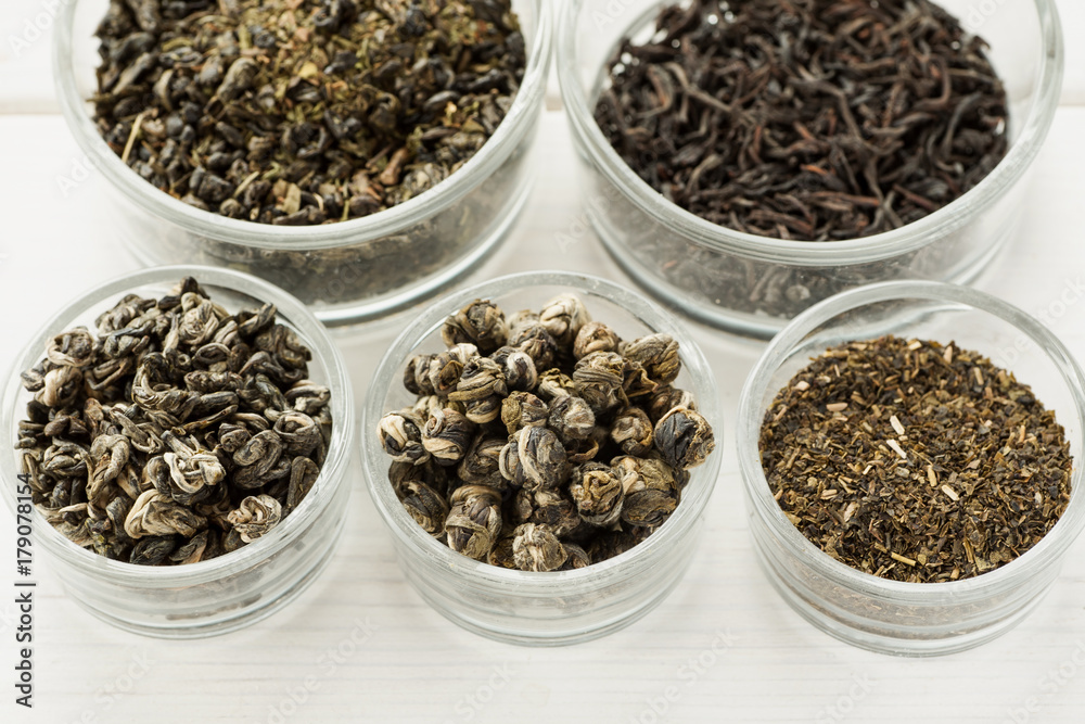 Different dry tea in a small glass dishes on a white wooden table Different dry tea in a small glass dishes on a white wooden table