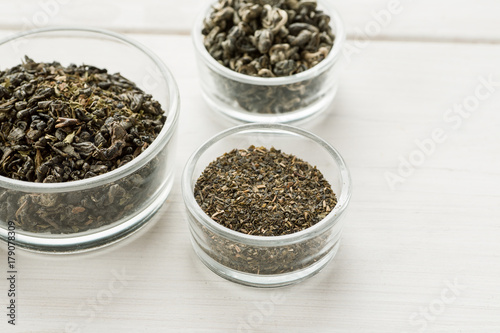 Different dry tea in a small glass dishes on a white wooden table