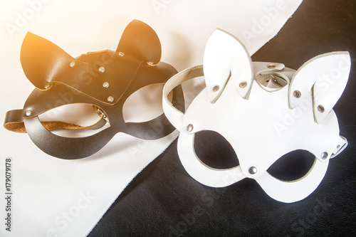 Close-up two handmade cat masks, hares of black and white color from genuine leather for masquerade, new year on black and white table
