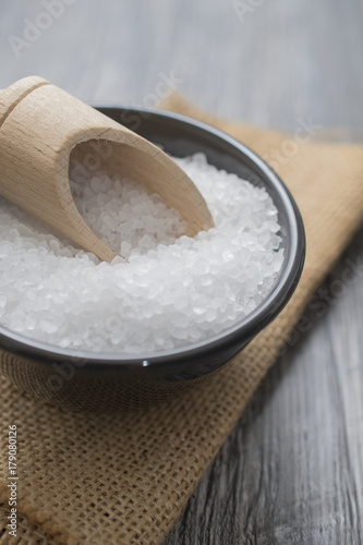 sea salt in the black bowl and with wooden spoon on wooden background.