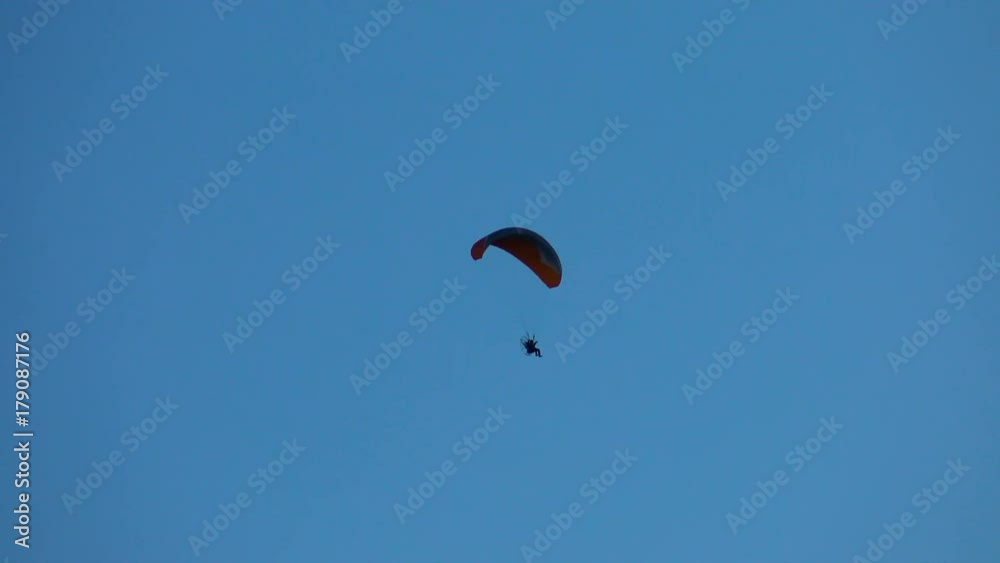 Paraglider flies in the blue sky. Air sport and recreation. A powered paraglider - a glider with a dorsal power plant, providing the rise and moving in the air. Paraglider flies in the blue sky. Air sport and recreation. A powered paraglider - a glider with a dorsal power plant, providing the rise and moving in the air.