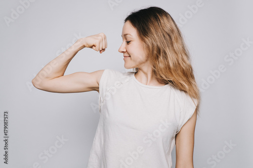 Fototapeta confident young sporty Caucasian woman in a white t-shirt showing biceps against
