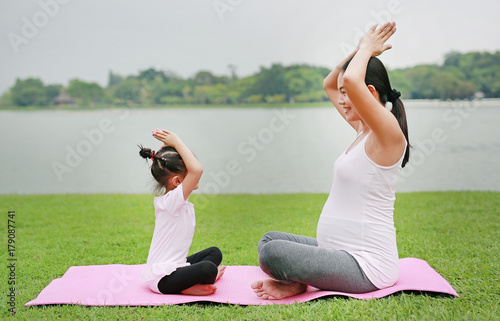 Pregnant mother and her daughter doing yoga in the public park.
