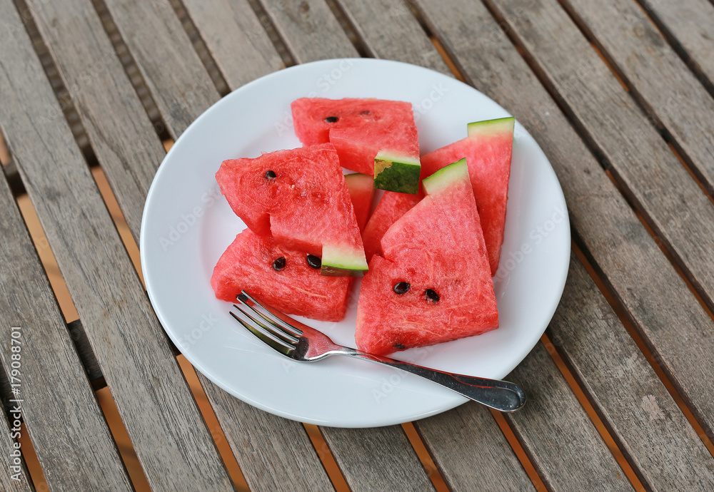 Fresh juicy watermelon slice on white plate on wooden table at restaurant.