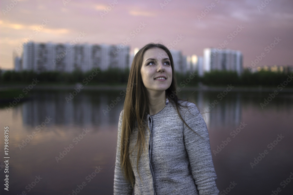 Young woman looks up at the sky on a sunset background. Lilac, pink sunset. Happiness. Laugh. Joy. Brunette