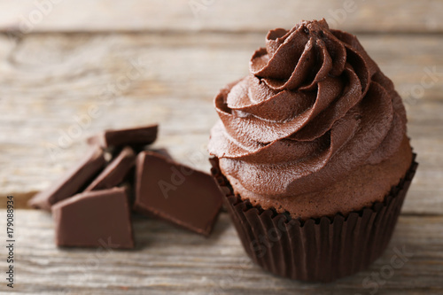 Tasty cupcake with pieces of chocolate on grey wooden table