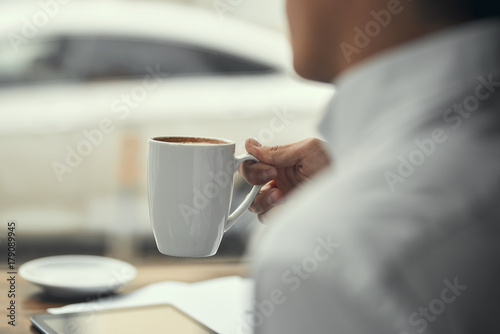 A guy in a white shirt, drinking coffee.