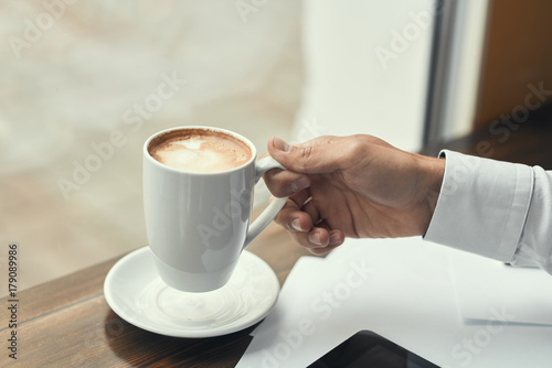 A guy in a white shirt  drinking coffee.