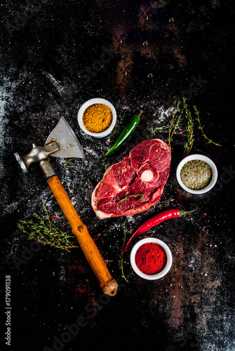 Fresh raw meat. A piece of lamb's tenderloin, with a bone, with a cutting ax, with spices for cooking on an old rusty black metal table Top view copy space