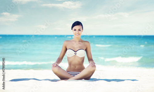Young  fit and beautiful girl meditating on a summer beach. Traveling  recreation  concept.