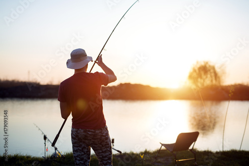 Papier peint Young man fishing on lake at sunset enjoying hobby
