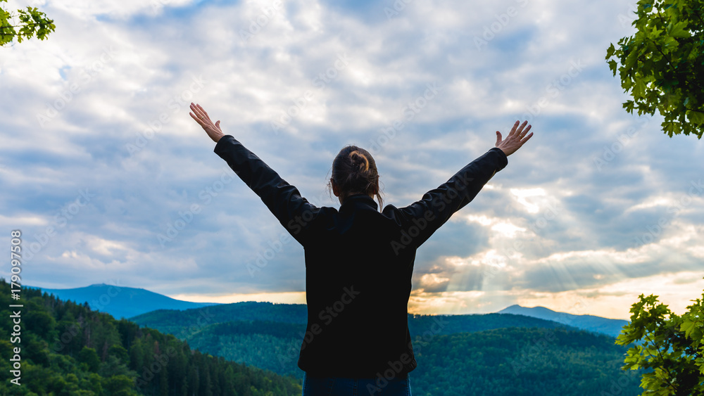 Hiker woman standing with hands up achieving the top, admiring mountain landscape. Epic shot of hiking with cloudy sky, freedom success concept Hiker woman standing with hands up achieving the top, admiring mountain landscape. Epic shot of hiking with cloudy sky, freedom success concept
