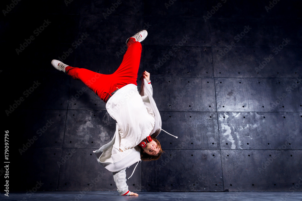 Male / man hip hop / r&b / break dancer dancing wearing in stylish modern red pants and  white coat handstand on industrial black background