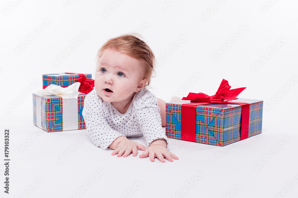 cute toddler is sitting in a New Year's red cap on white background unpacks a gift with a smile on his face cute toddler is sitting in a New Year's red cap on white background unpacks a gift with a smile on his face