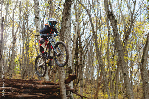 a young rider at the wheel of his mountain bike makes a trick in jumping on the springboard of the downhill mountain path in the autumn forest