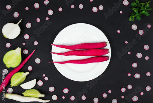 radish on a plate of long pink, on a black background vegetables,