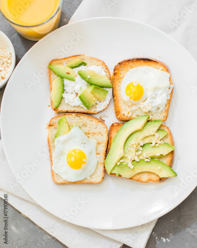 Breakfast. Eggs on toast with avocado, soft white cheese, spices and nuts. White plate, gray concrete background.