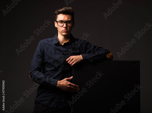 Young confident man portrait of a businessman showing presentation, pointing paper placard black background. Ideal for banners, registration forms, presentation, landings, presenting concept.