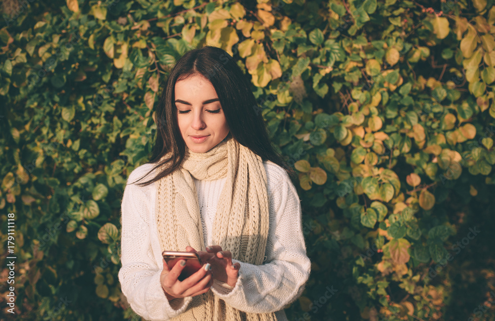 Woman using smartphone in fall. Autumn girl having smart phone conversation in sun flare foliage. Portrait of Caucasian model in forest in fall colors. Woman using smartphone in fall. Autumn girl having smart phone conversation in sun flare foliage. Portrait of Caucasian model in forest in fall colors.